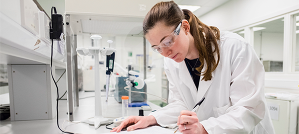 женщина в лабораторном халате пишет на бумаге