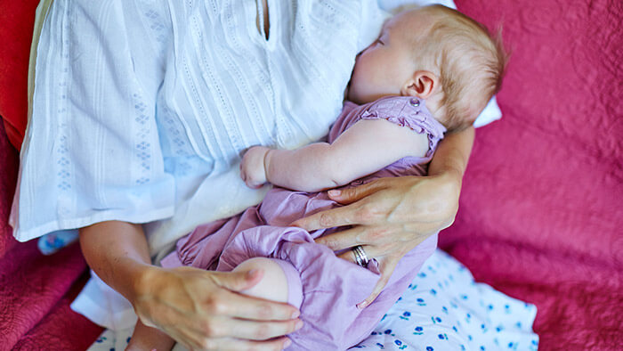 Мама в свободной одежде кормит грудью ребенка. Одна из причин закупорки молочного протока &ndash; тесная одежда и бюстгальтеры.
